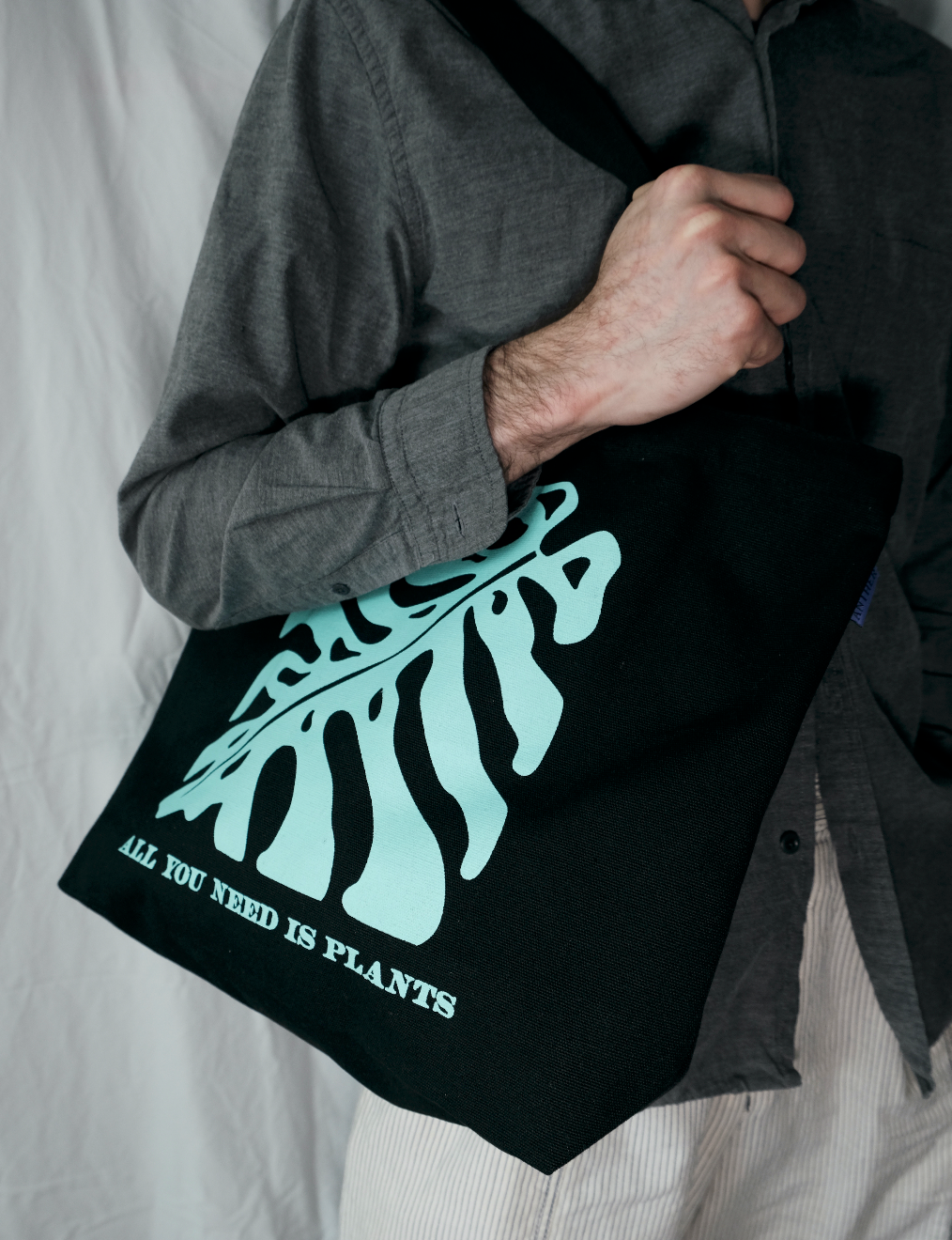 Person holding a black tote bag with tropical plant design and text.